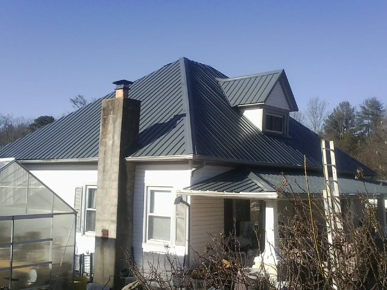 Dark blue standing seam metal roof on a white farmhouse with dormer — Slate & Tile Roof Repair by Roofing Brothers in Selkirk