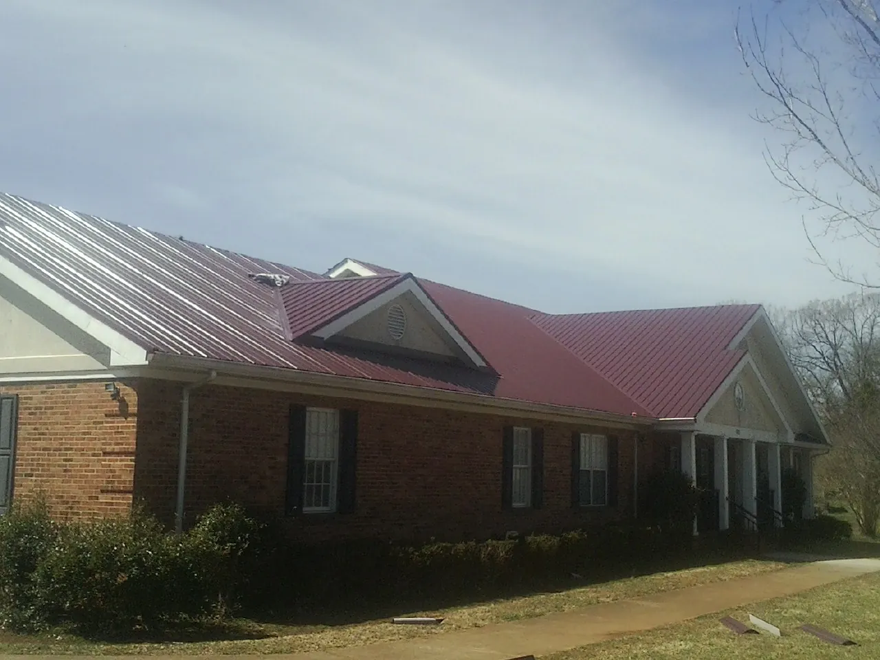 Red metal roof with gabled entries on a long brick building, from a Hail Damage Roof Repair job in Selkirk