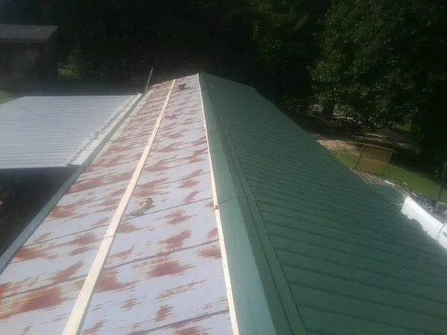 Old rusted panels beside newly installed green metal roofing — Wind Damage Roof Repair by Roofing Brothers in Selkirk