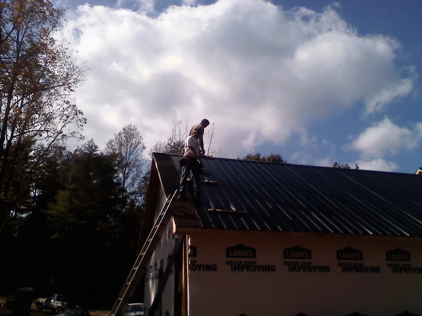 Roofer fastening dark metal panels high against a cloudy sky, from a Roof Inspection job in Selkirk