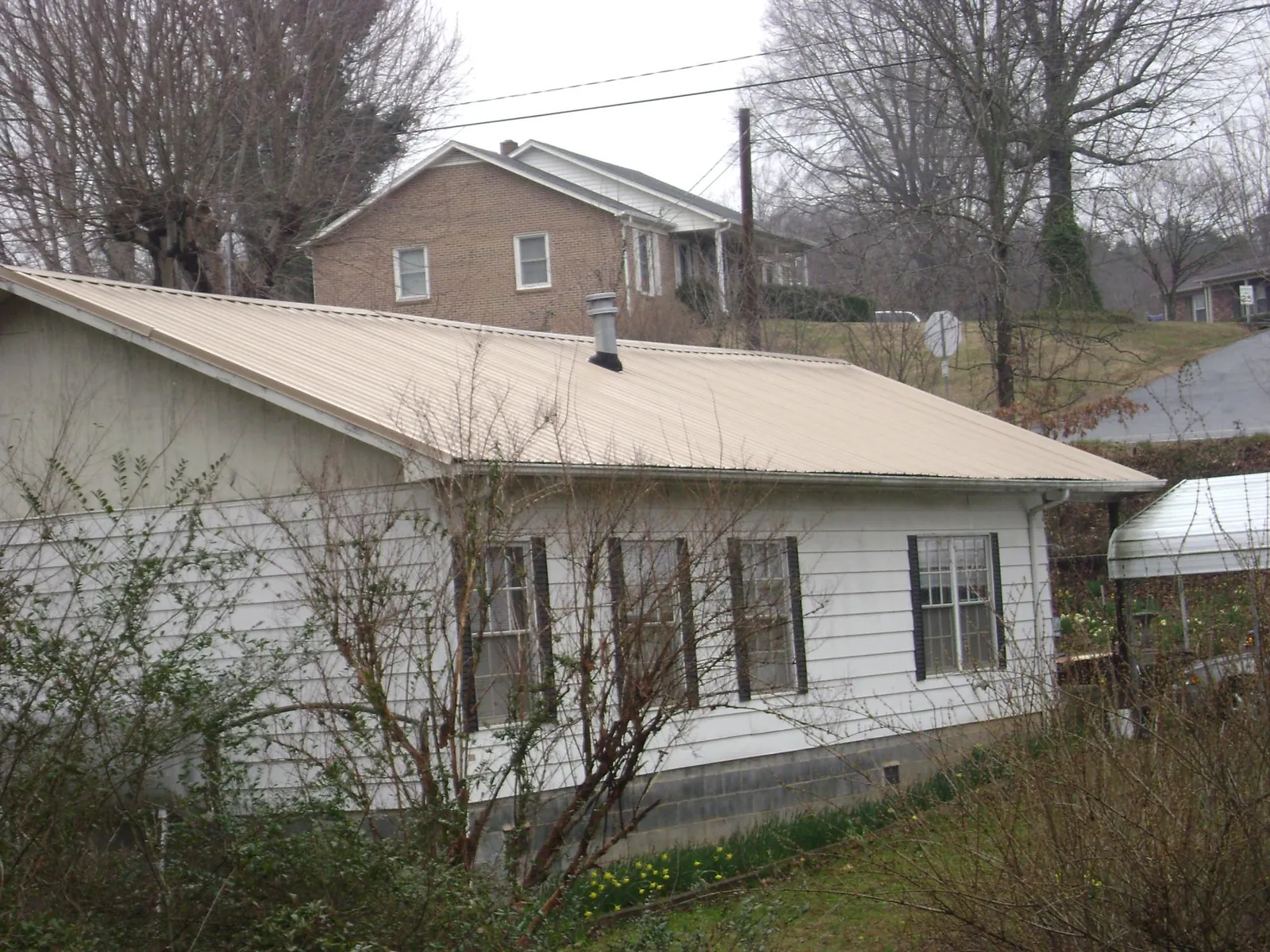 Tan metal roof on a white sided house set into a hillside — Commercial Roofing by Roofing Brothers in Selkirk