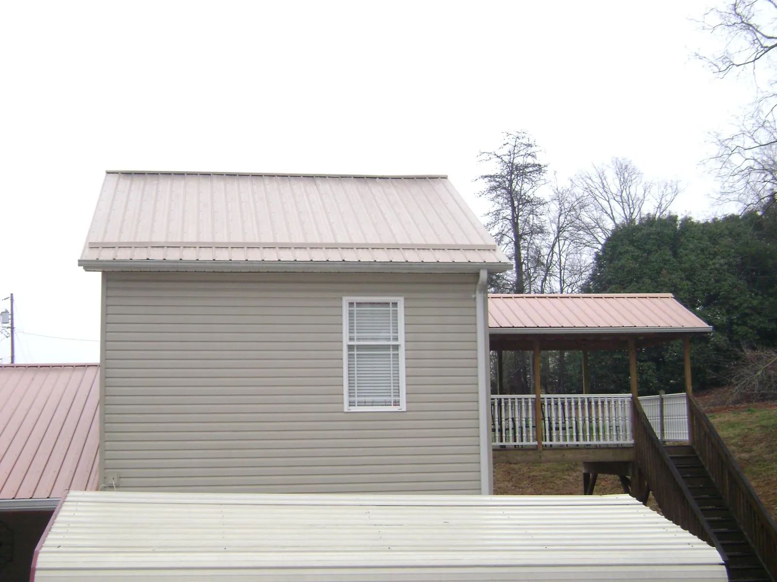 Tan metal roofs on a two story addition and attached porch, from a Roof Replacement job in Selkirk